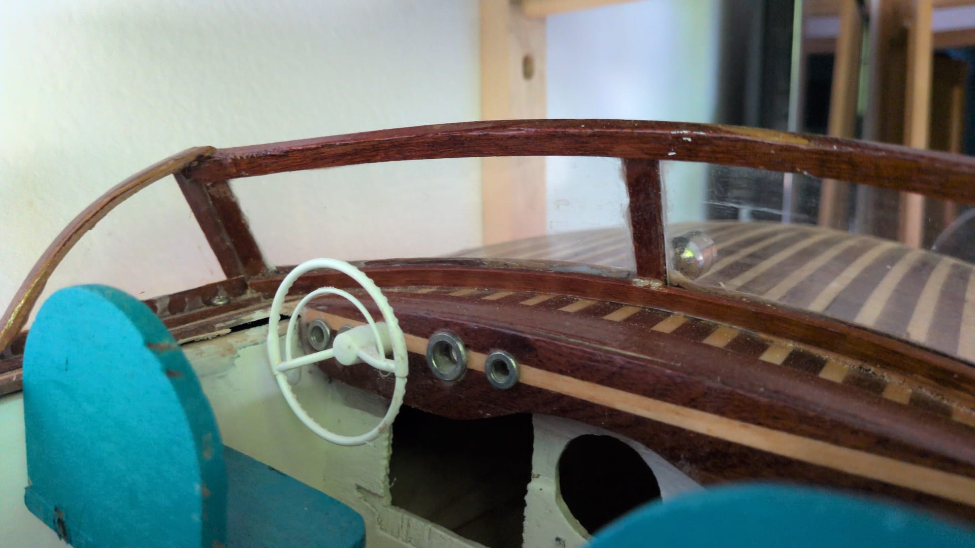 Interior de la cabina de una lancha clásica: volante blanco, asientos turquesa y salpicadero de madera