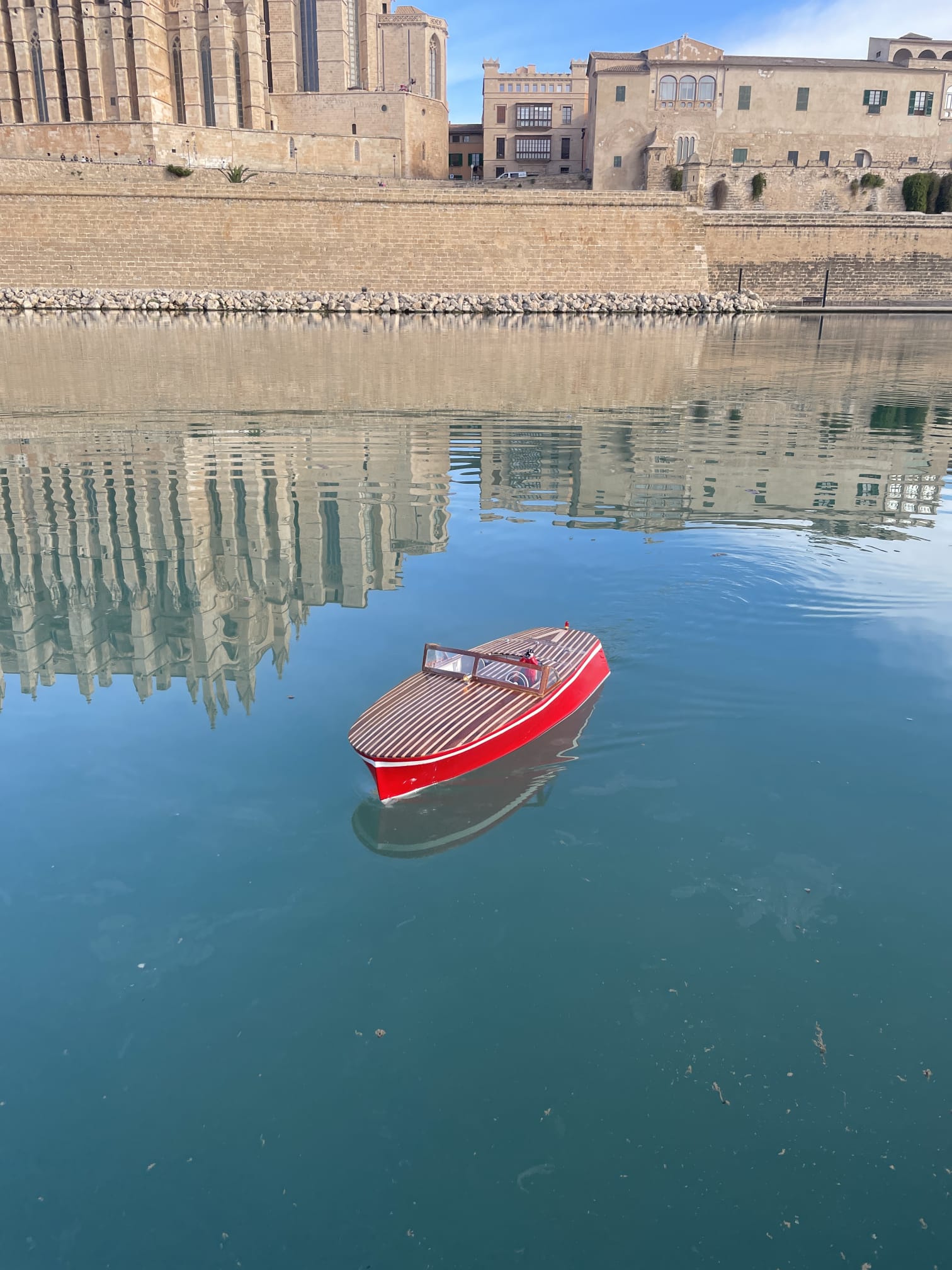Lancha clásica de radiocontrol de casco rojo navegando en el Parc de la Mar, con la Catedral de Palma al fondo