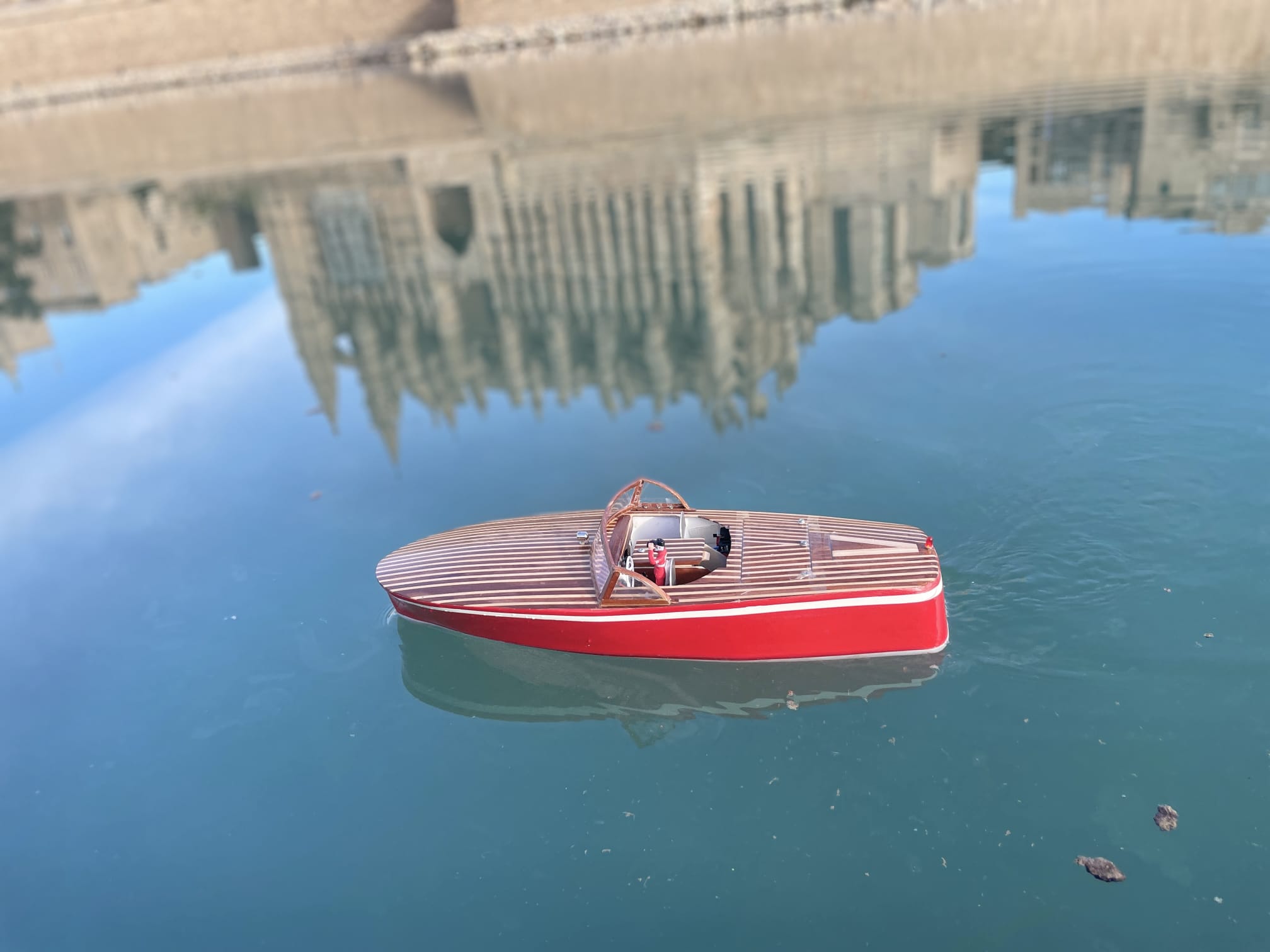 Runabout rojo de radiocontrol sobre el agua turquesa del Parc de la Mar con reflejos de la ciudad