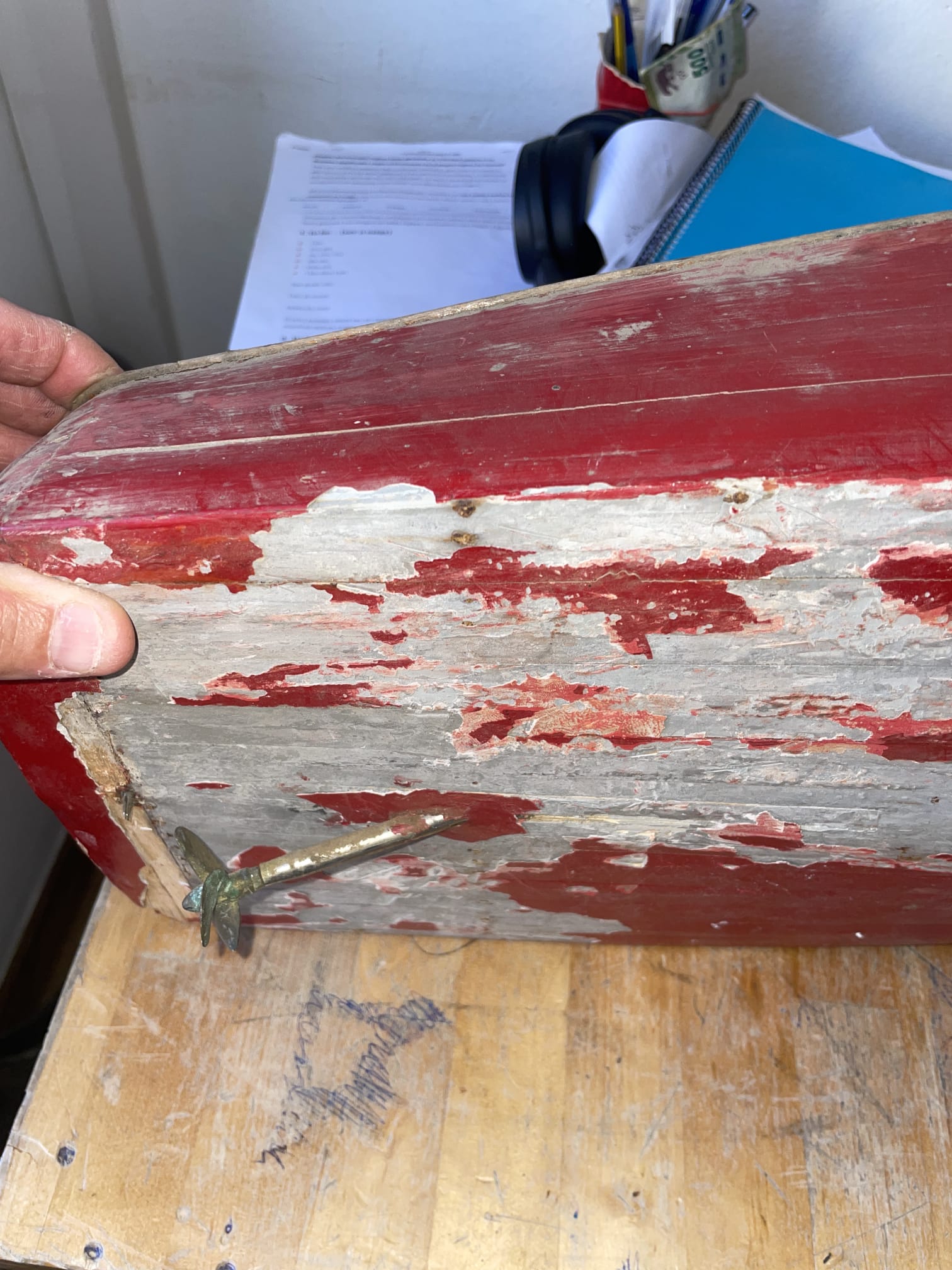 Casco antiguo con la pintura roja saltada y la hélice de latón, sostenido en la mano
